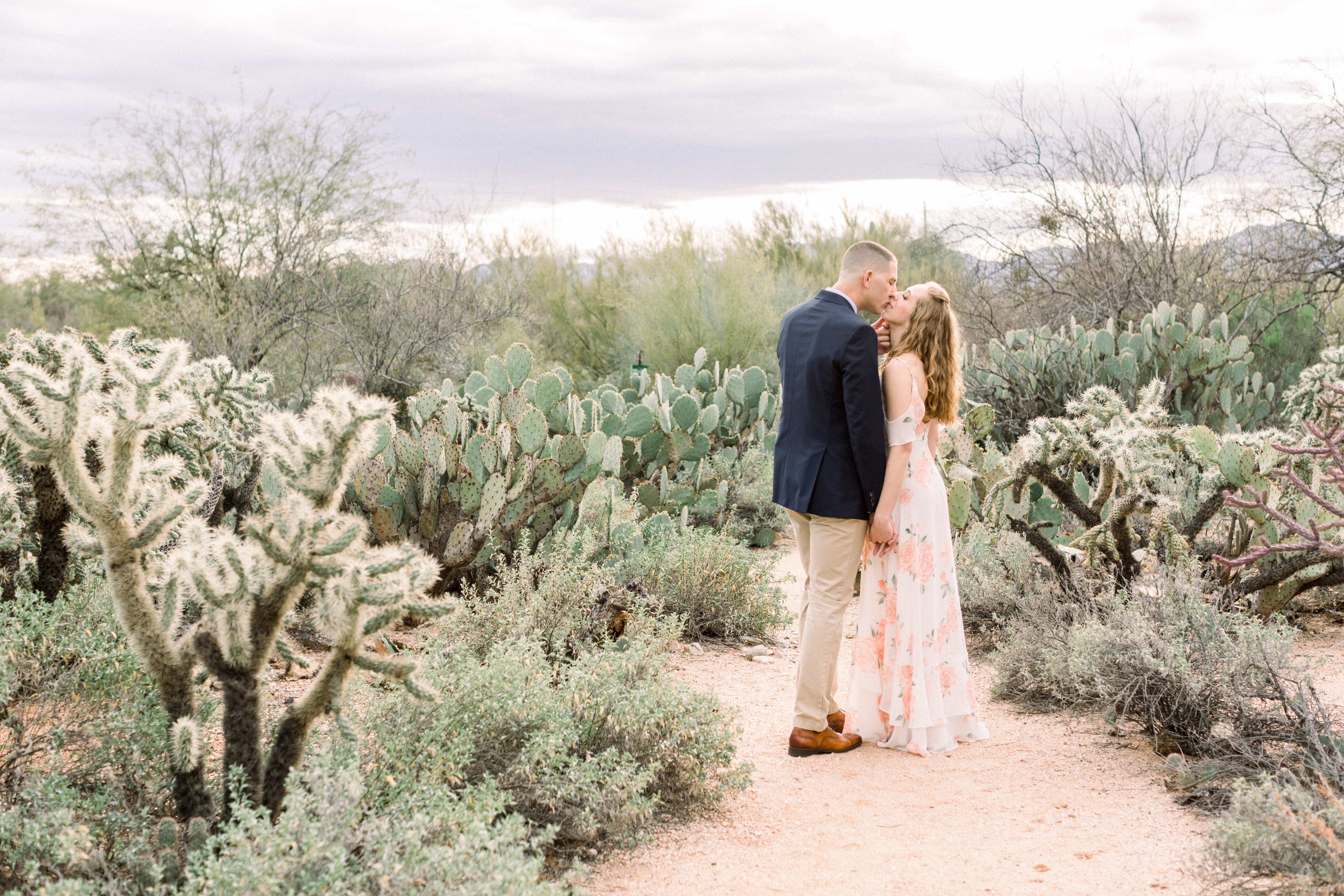 Tohono Chul Park Engagement Session with a woman in a flowery dress and man in a suit, kissing. Photo by Amber Lea Photography.